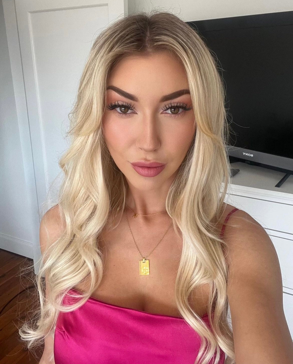 Woman with long curly blonde hair wearing a pink top showcasing Extra Piece Buttercream Blonde 