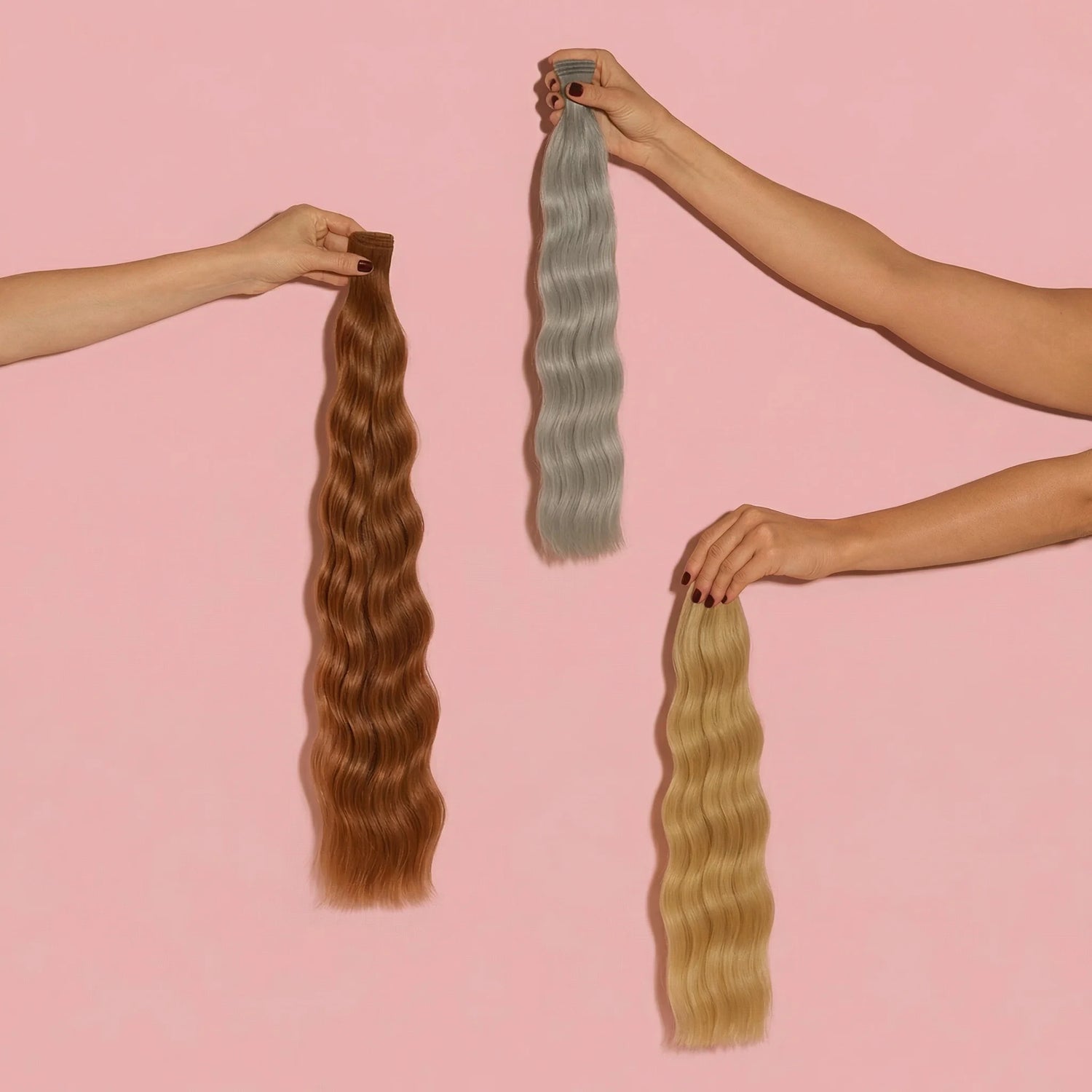Three hands holding three long wavy hair extensions in brown, gray, and blonde shades against pink background