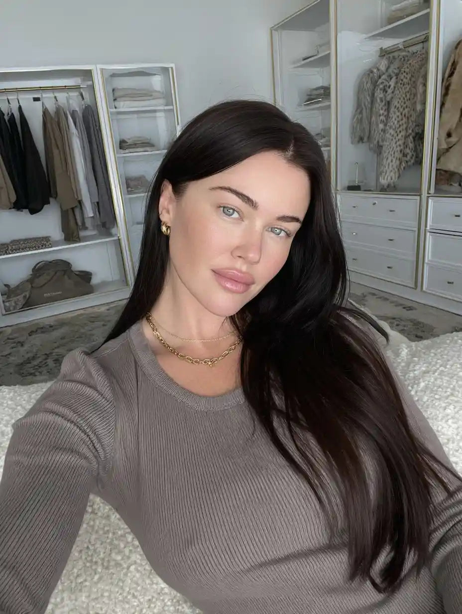 Woman with long dark hair wearing a taupe ribbed top taking a selfie in a modern bedroom closet setting